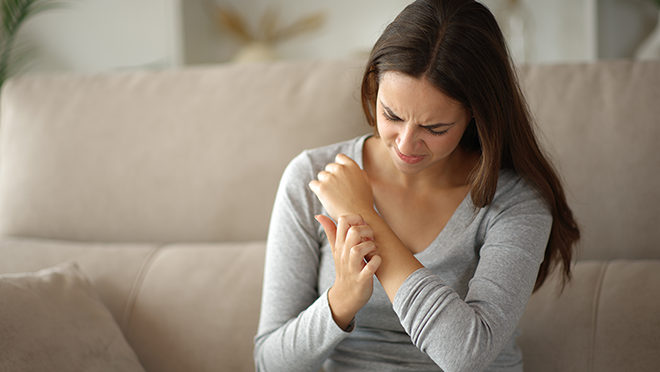 A woman looking down at her arm in irritation and scratching.