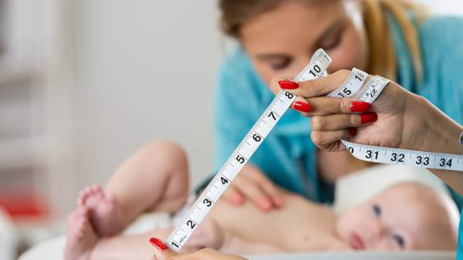 A woman with red nails holding a measuring tape in her hands with a baby and another woman blurred in the background