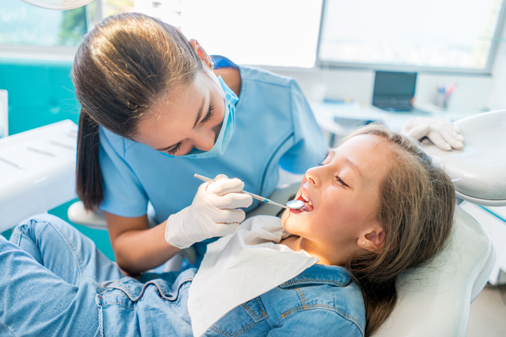 Young girl lies in dental chair while dental care professional examines her teeth