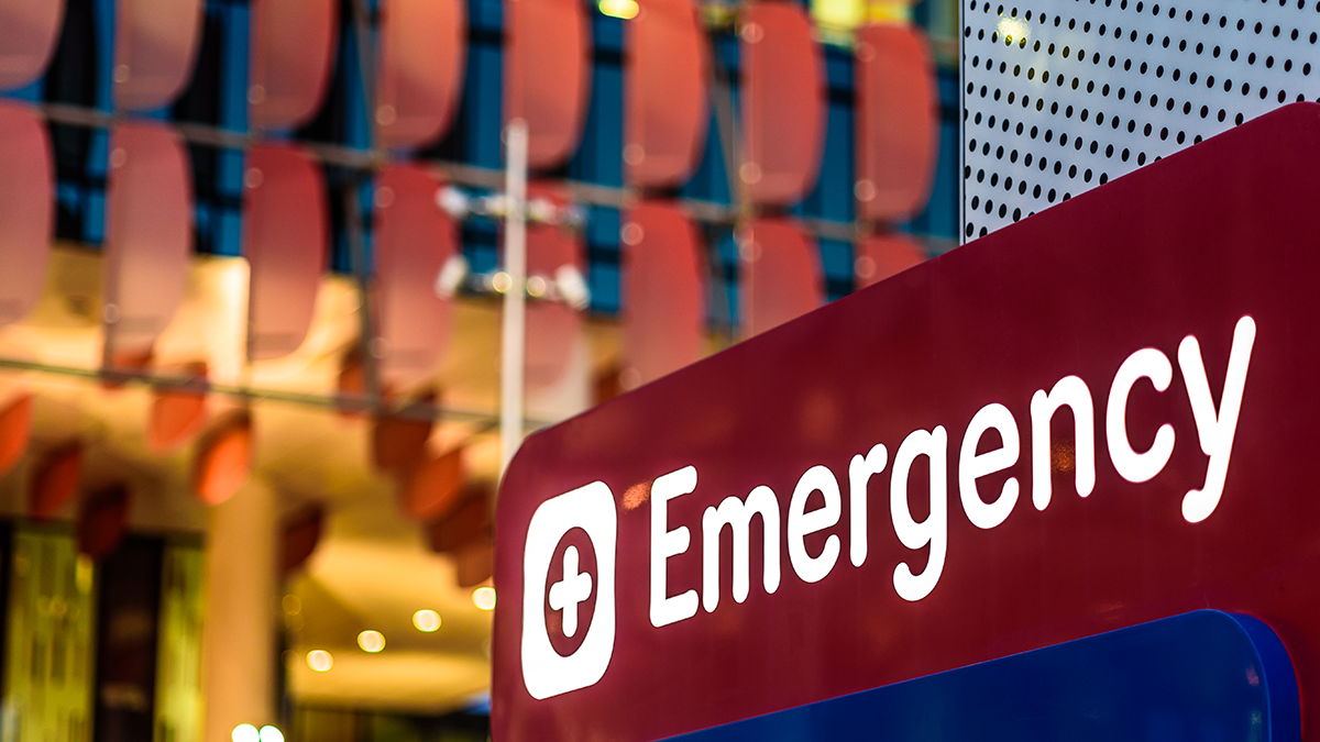 Red and white emergency sign featuring a white cross on a red circle in front of a building
