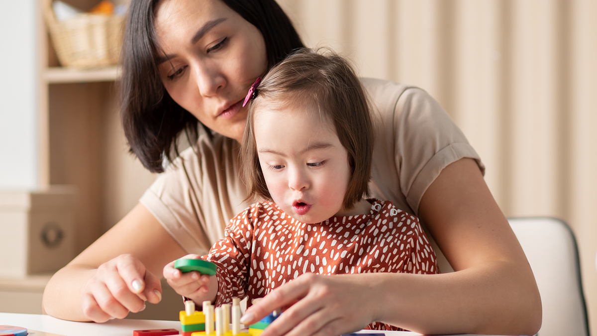 Mother and child, the latter with an intellectual disability, sit together playing with a toy
