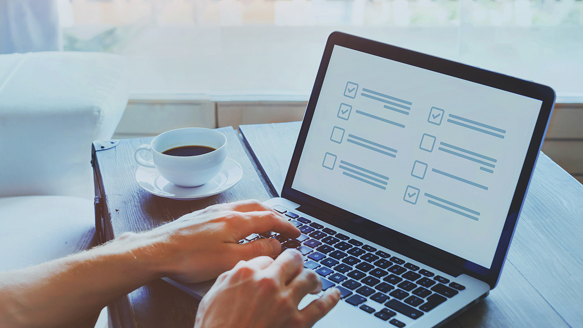 Laptop and cup of coffee on desk, hands reach from offscreen to laptop to answer questions on screen