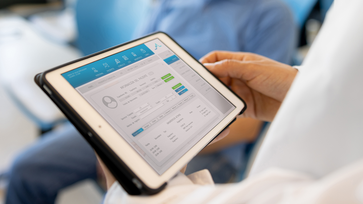 Torso in white coat holds a tablet showing a medical record while body of patient sits behind it