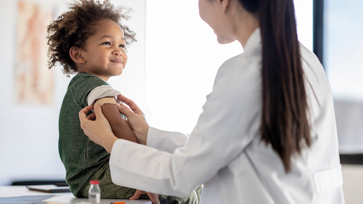 Female doctor applies post-vaccination bandage to the arm of a smiling little boy