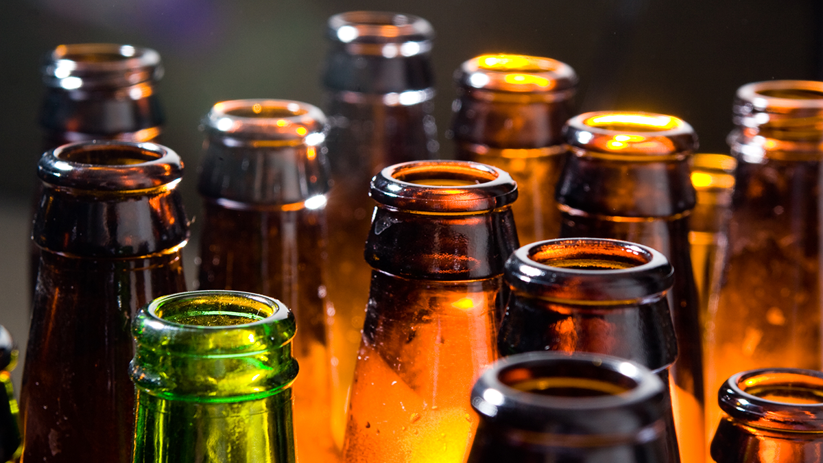 Light shines on a close up on the necks of amber and green beer bottles
