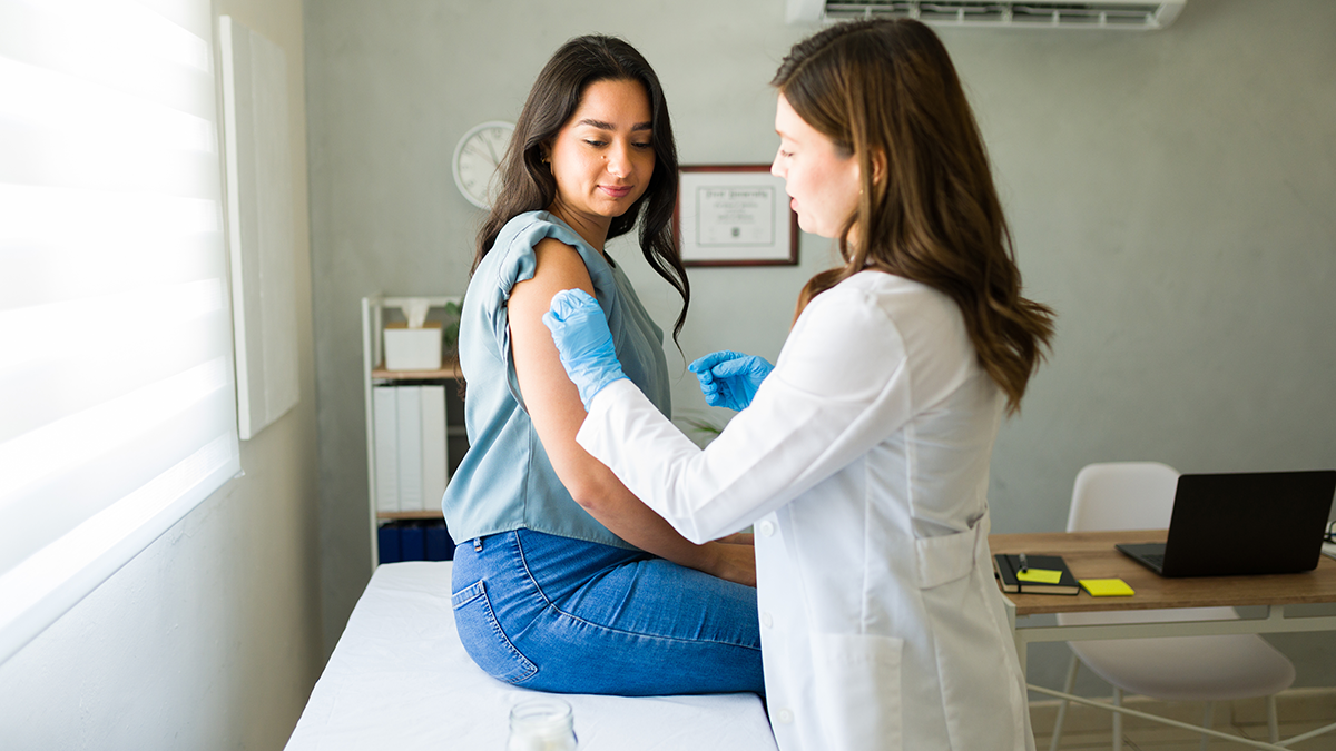 Female doctor swabs arm of young adult female patient before administering vaccine