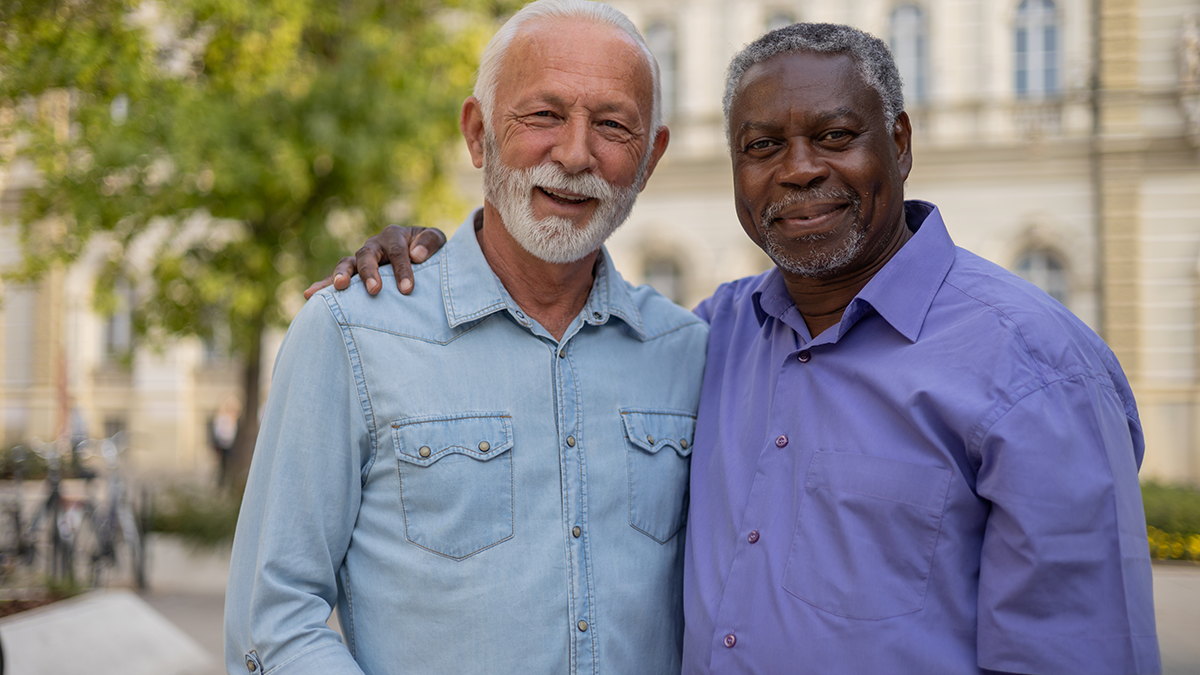 Older white and black men stand together with arms around each other on a city street