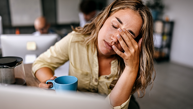 A woman holding a coffee cup and rubbing her eyes in expressed tiredness.