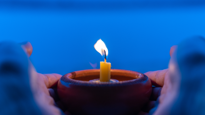 Person holding a container with a small candle burning inside as a memorial tribute.