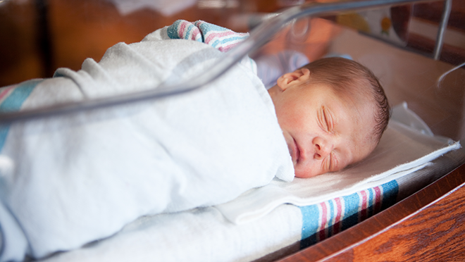 Newborn baby sleeping in hospital nursery.