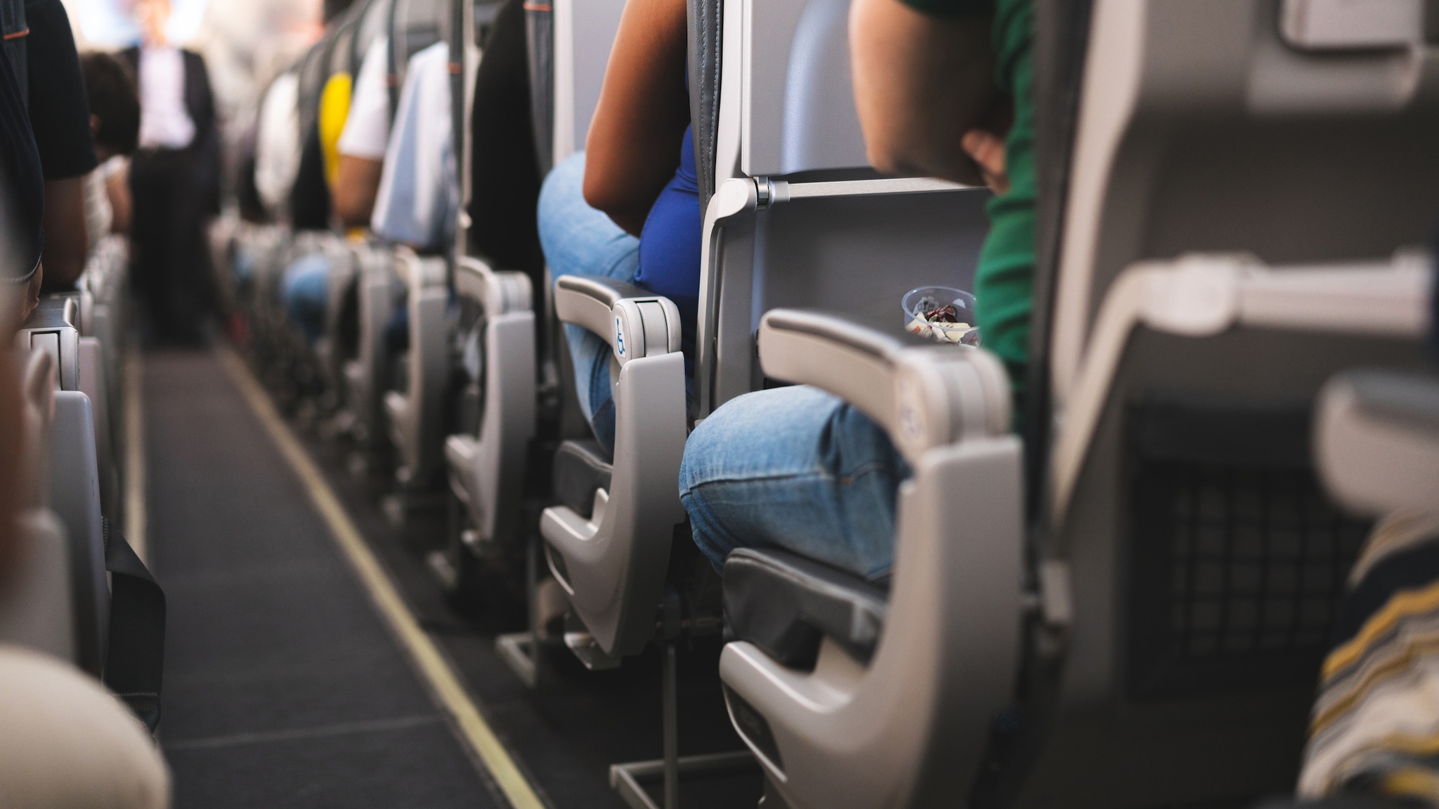 Inside of a commercial aircraft and passengers shown from the rear of the cabin.