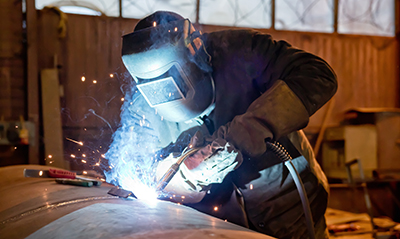 A welder in a hood and protective gear welds a seam.