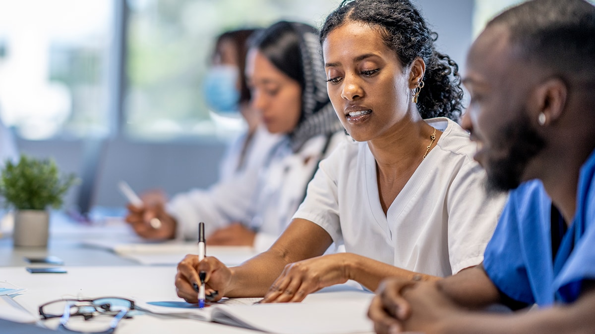 Row of adult students in scrubs sitting along one side of a table.