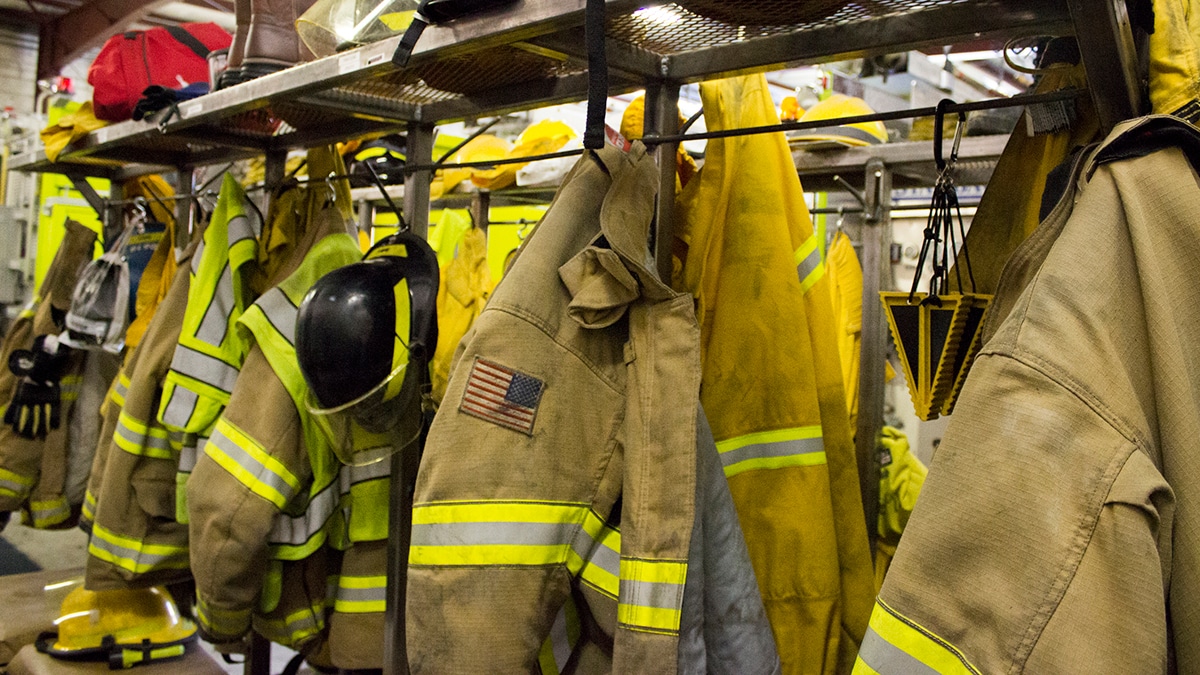 Photo showing multiple Firefighter coats, hats, equipment hanging up.