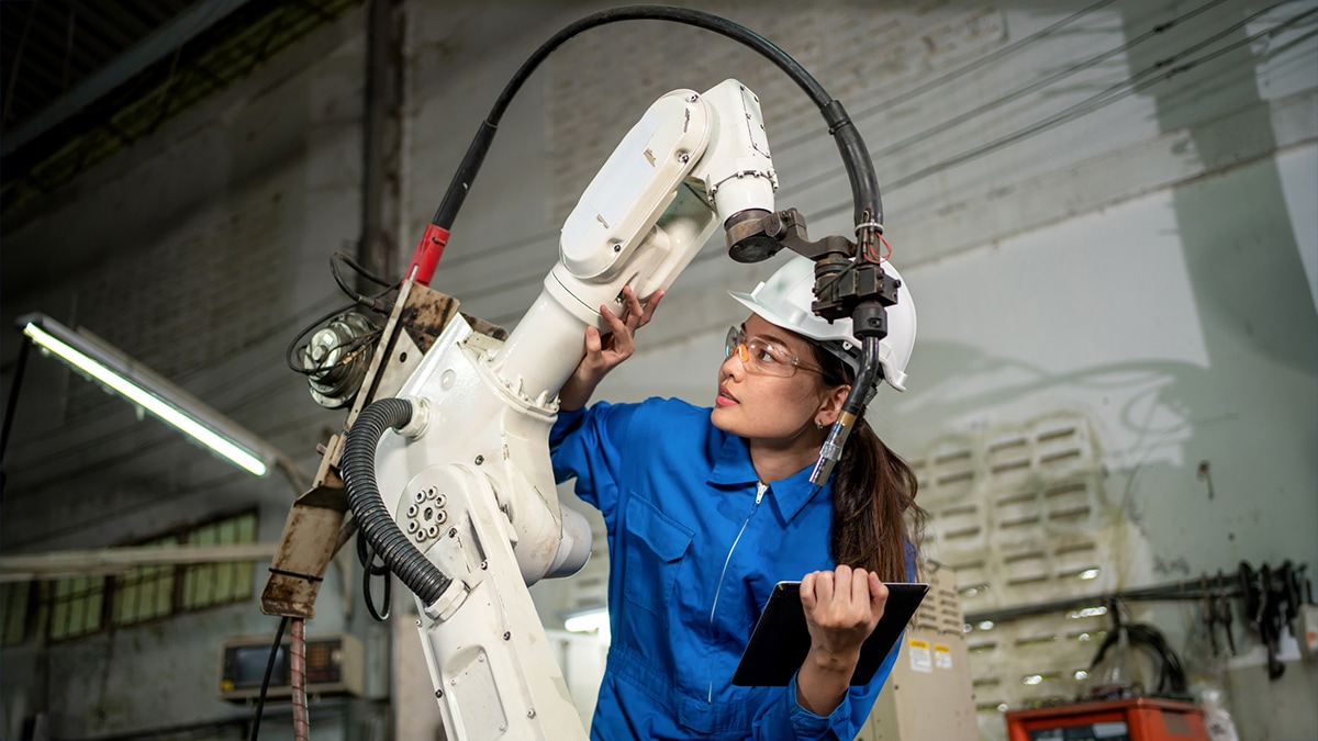 Photo of a young black woman with a hard hat working near a robot.