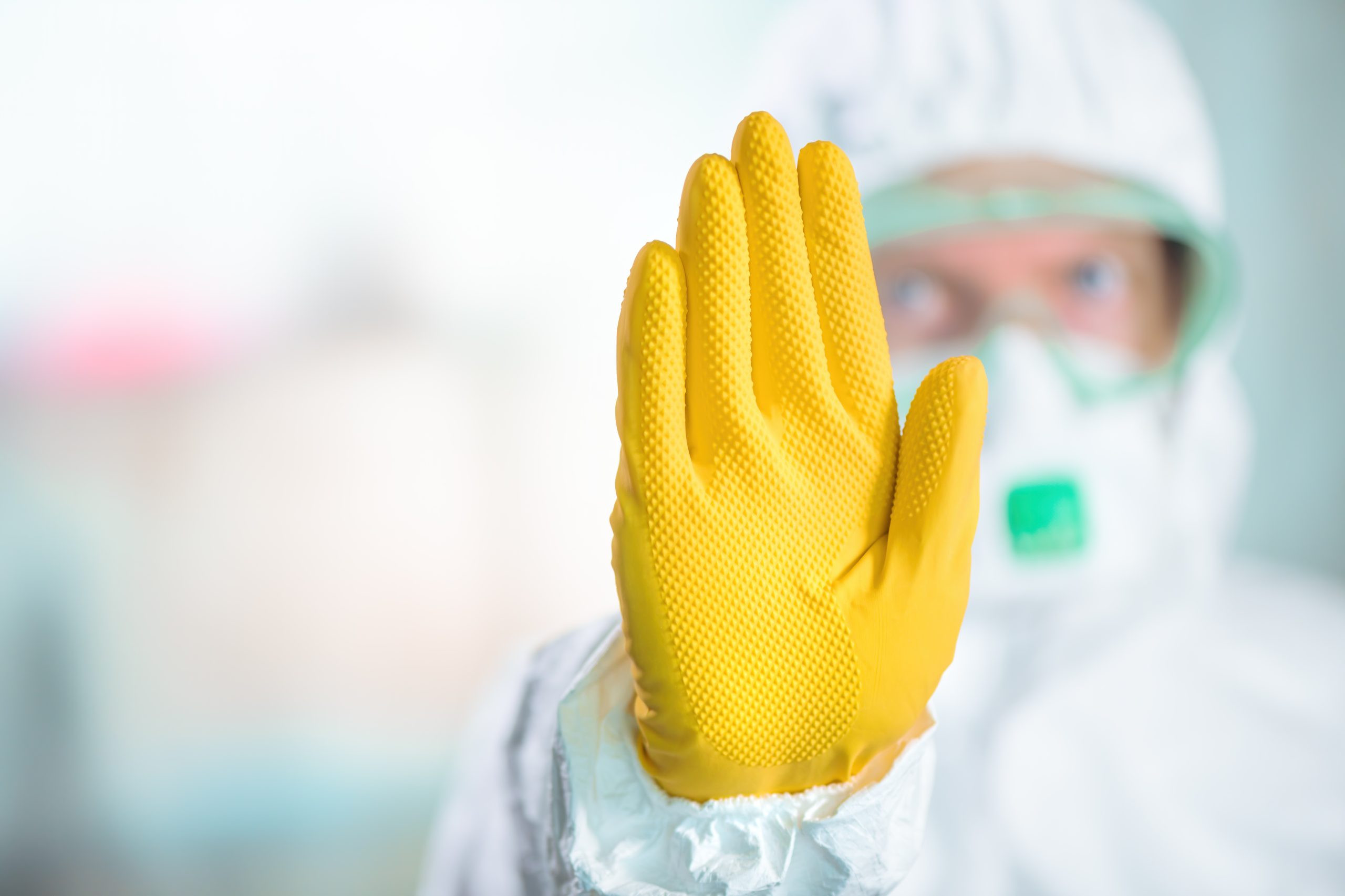 Female in PPE wearing yellow glove gesturing stop sign in hospital quarantine.