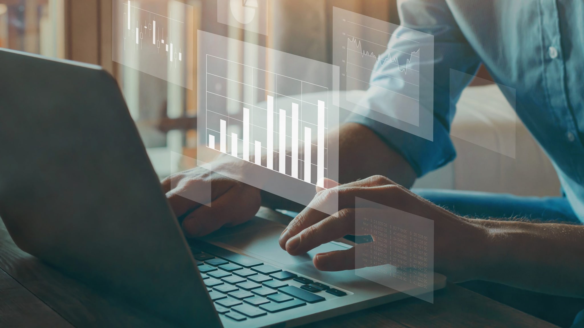 Hands typing on a laptop with small, transparent charts and graphs.