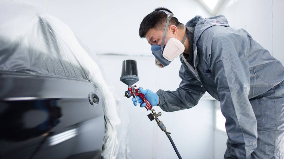 Worker wearing an elastomeric half mask respirator while spray painting a car