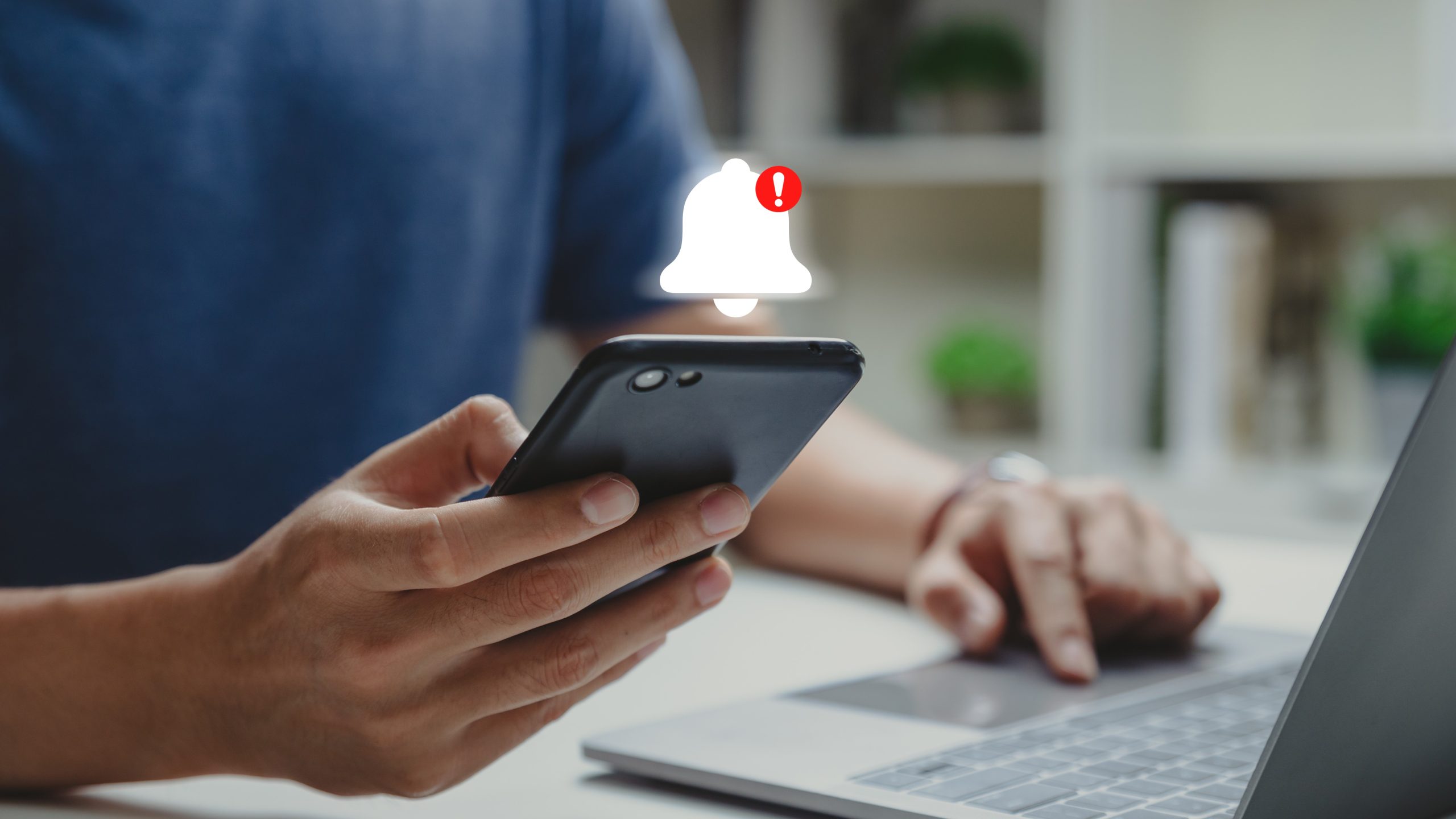 Person on their phone and computer. Notification bell above phone.