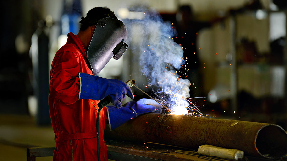 A welder working on a pipe with sparks flying.