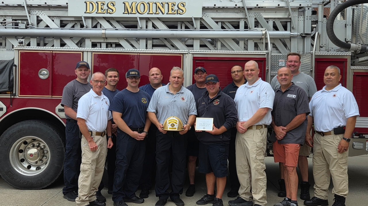 Group of firefighters in front of a fire truck holding a gold helmet