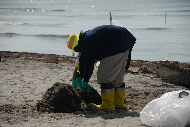 A person in a reflective hat and gloves, bending over, cleaning up on the beach