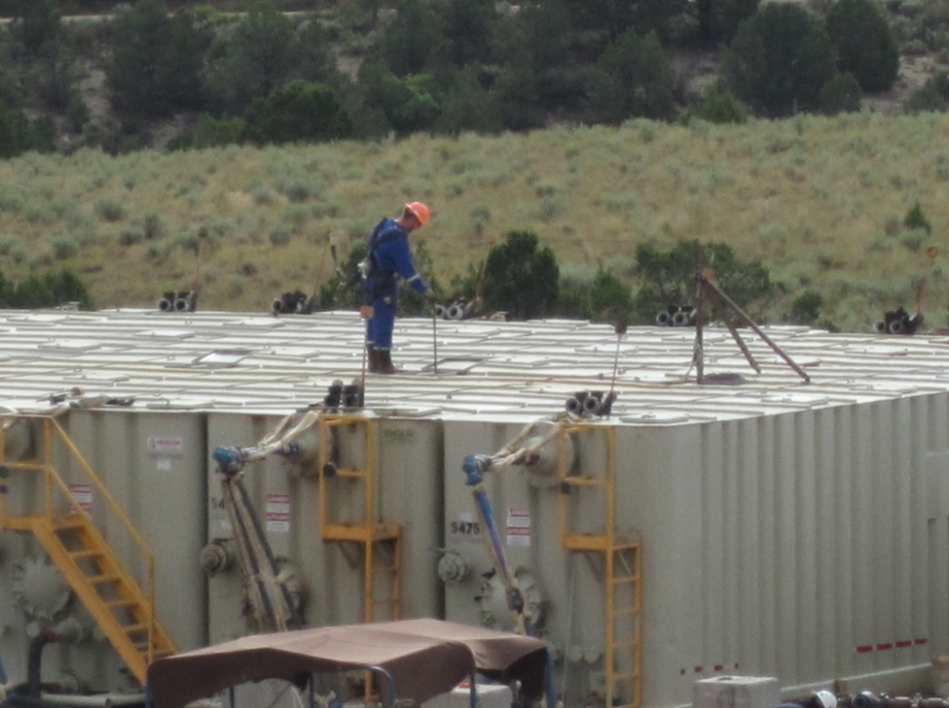 A flowback technician gauging a flowback tank through a hatch on top of the tank