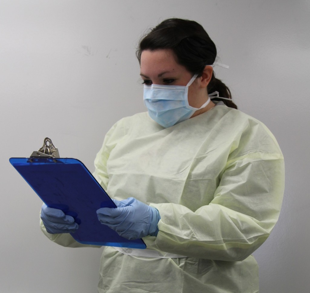 woman wearing yellow gown with blue gloves and mask holding a clipboard