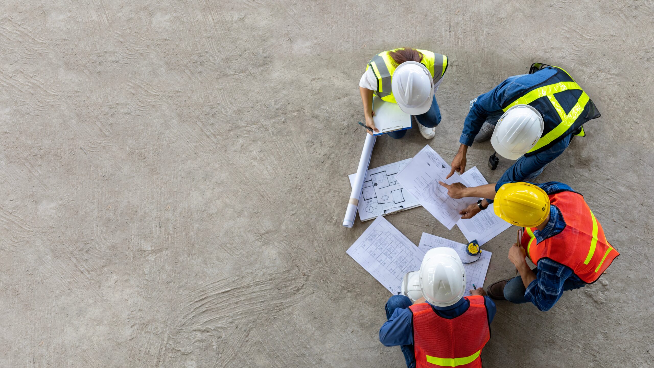 Birds-eye view of four people on a construction site looking at blueprints
