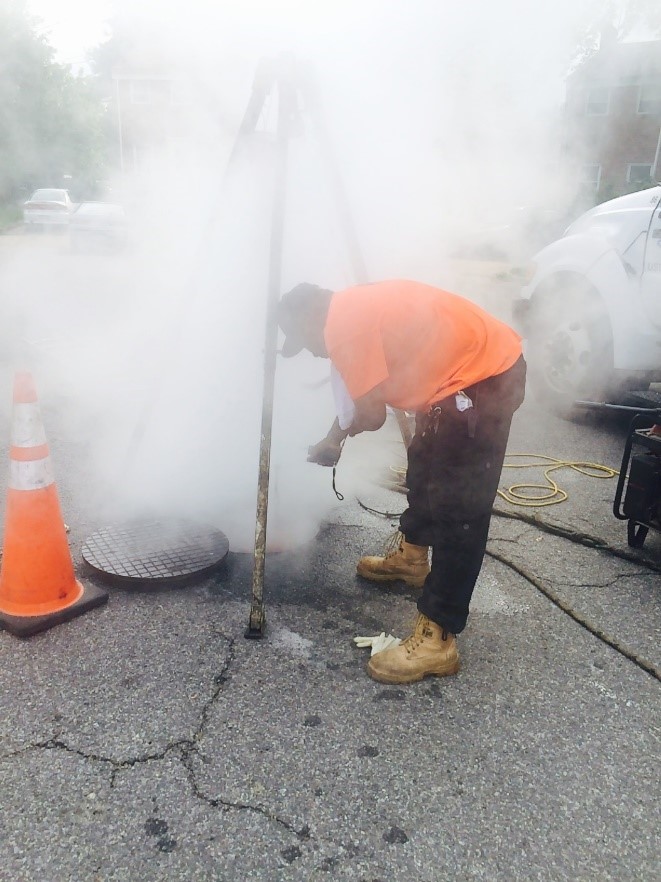 Image of a worker without respiratory protection inspecting a CIPP emission point at a sanitary sewer pipe manhole.