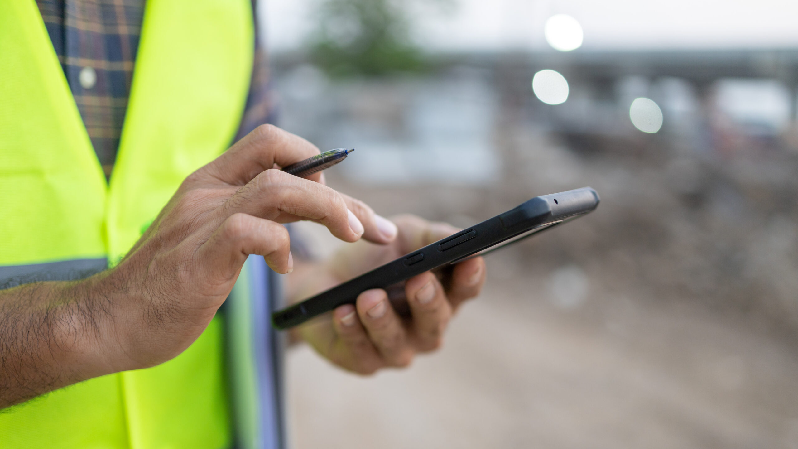 Close up of a man in safety vest using a mobile phone on a construction site.