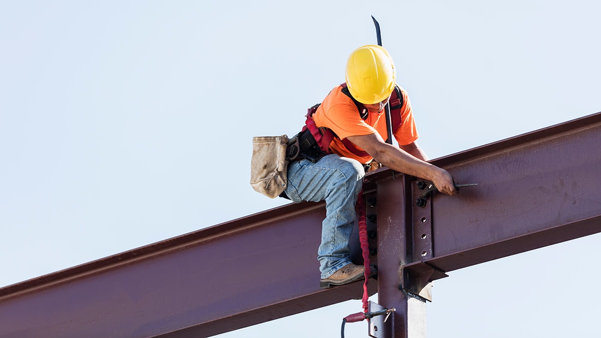 Construction worker on beam wearing hard hat.