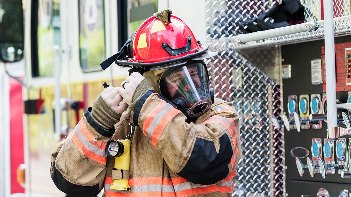Firefighter in full gear adjusting the strap of their respirator.