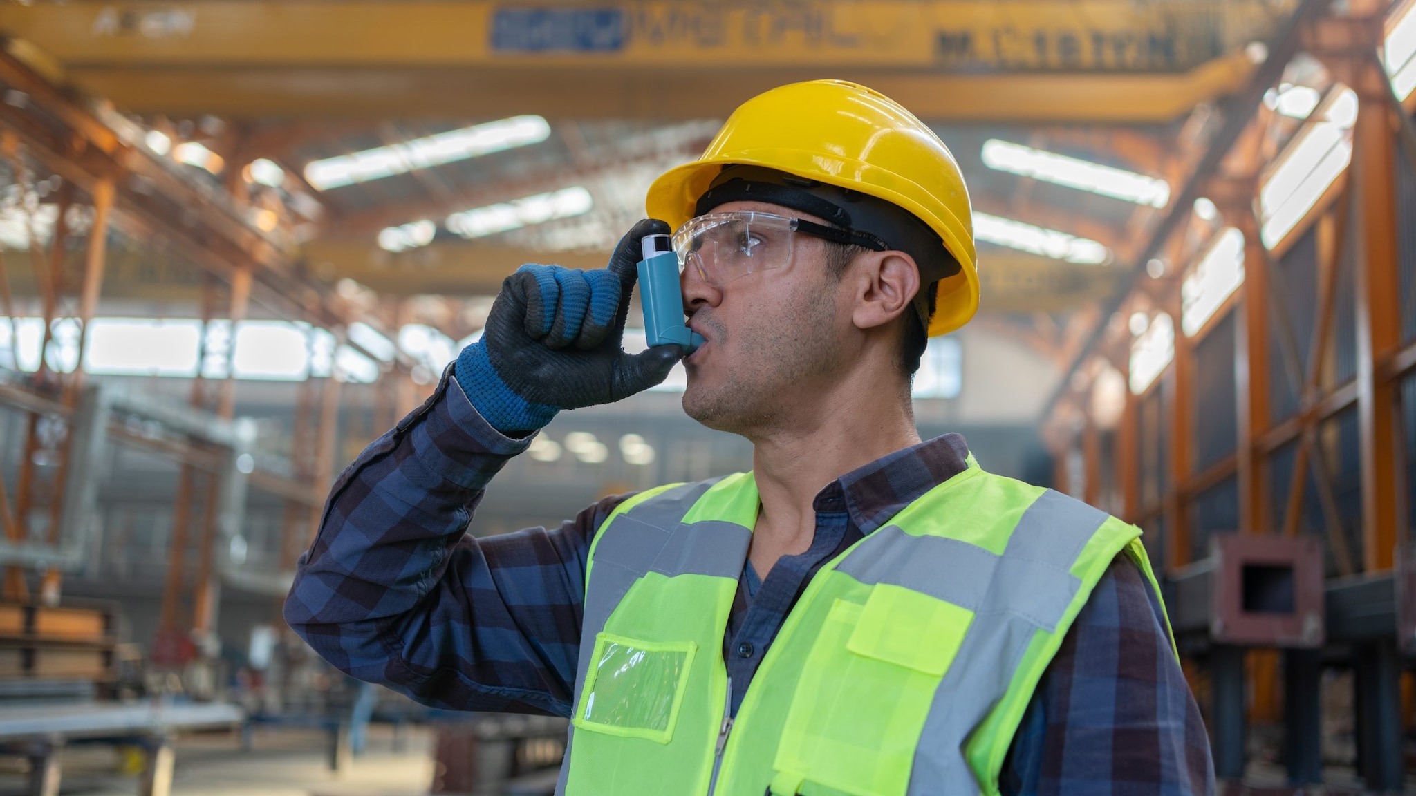 Industrial worker wearing a hard hat using an inhaler.