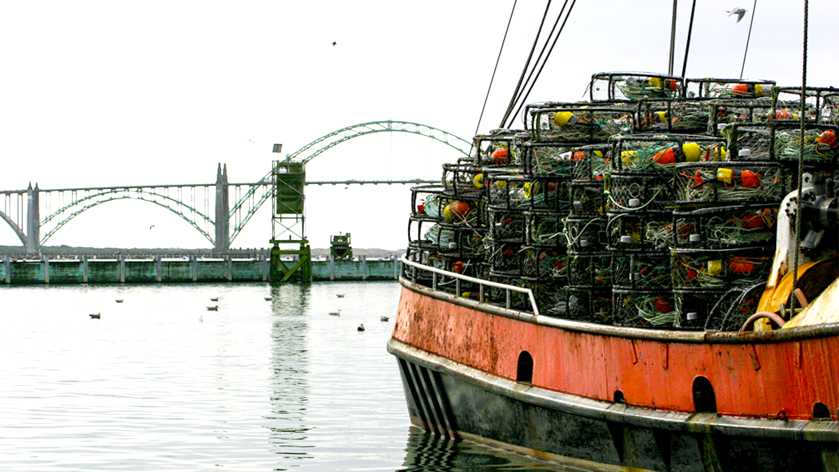 An image with a Dungeness crab vessel loaded with pots in the foreground and the Yaquina Bay Bridge in the background. Photo by NIOSH