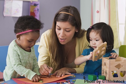 M10F A female preschool teacher helps two girls color and construct with building blocks