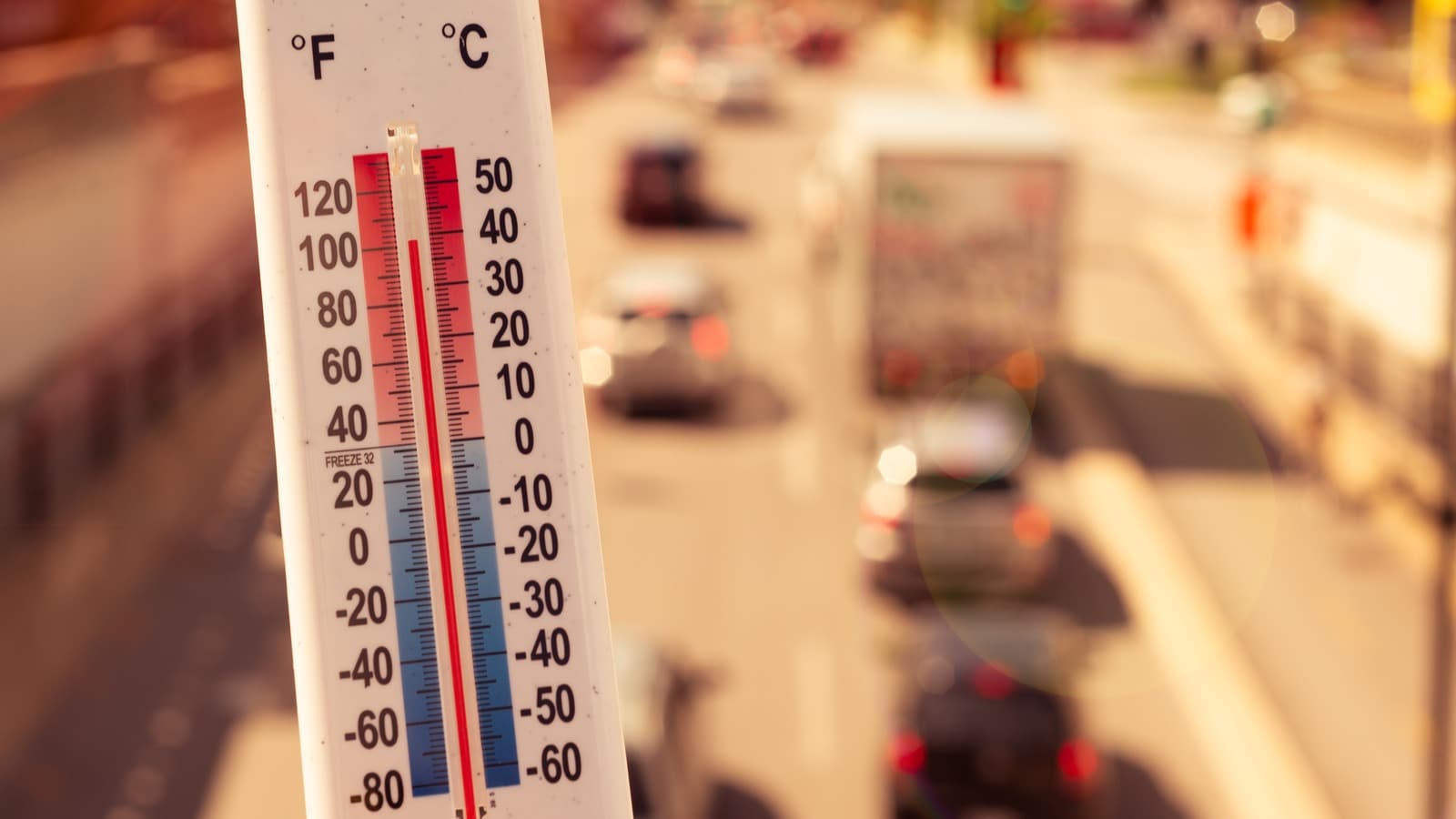 Extreme heat visualized in front of traffic with a thermometer.