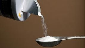 Closeup photo of salt being poured into a measuring spoon.
