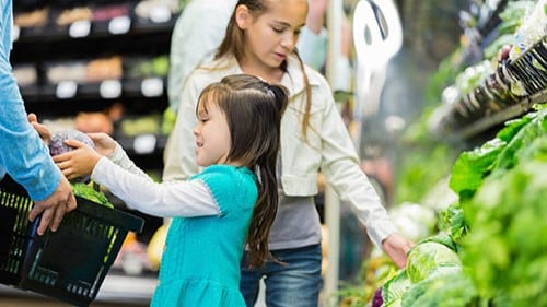 Two girls shopping for vegetables at grocery store.