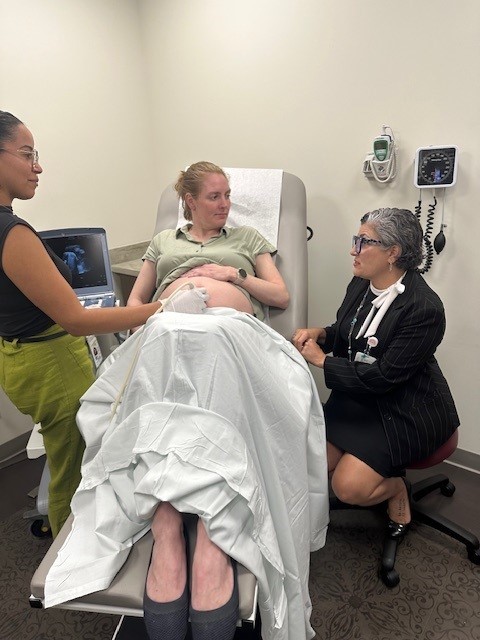 Photo of a pregnant woman in a medical chair speaking to a female doctor as another woman does an ultrasound