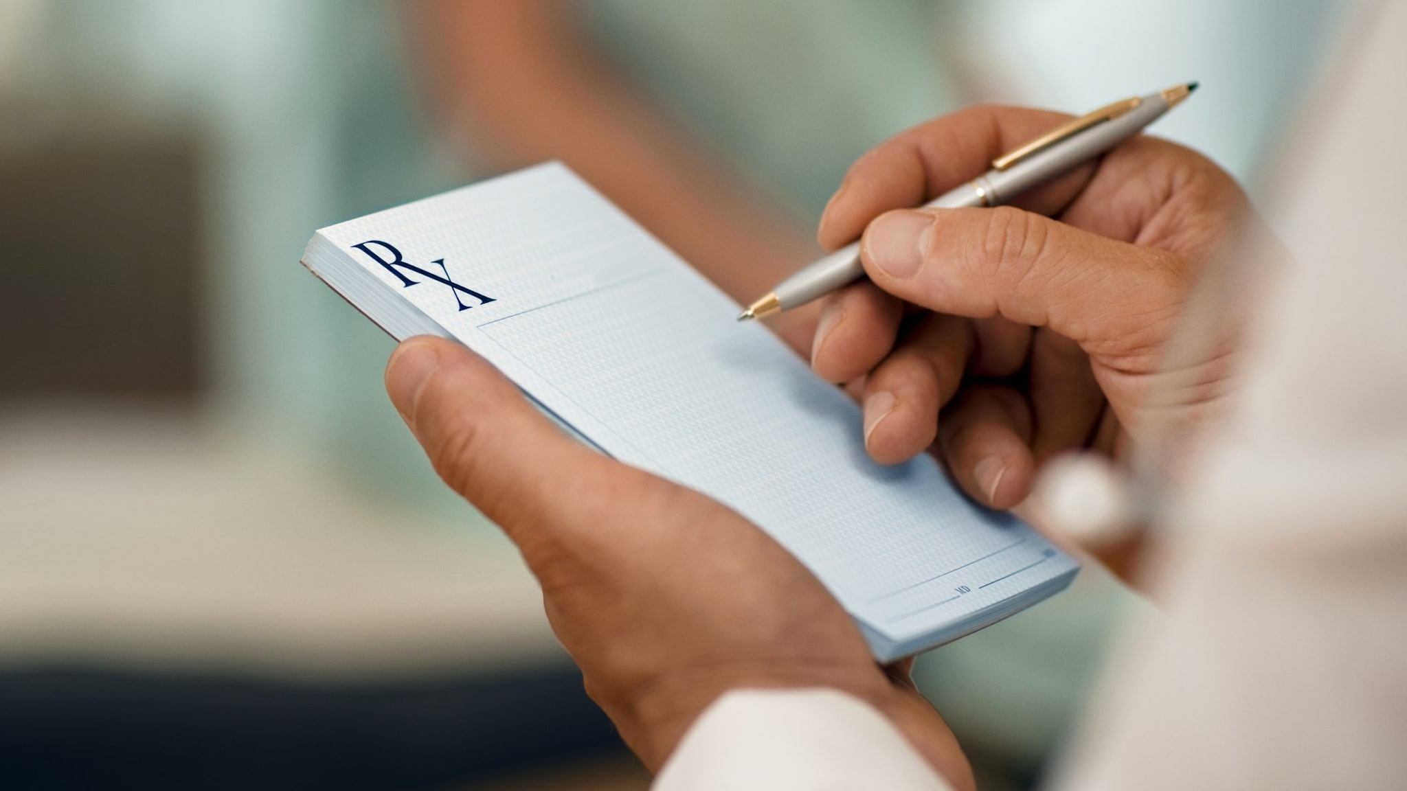 A closeup of a clinician's hands holding up a prescription pad and pen.