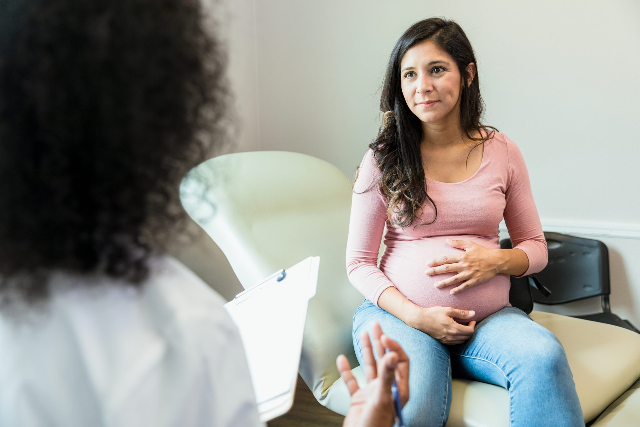 Clinician and pregnant patient talking in an exam room.