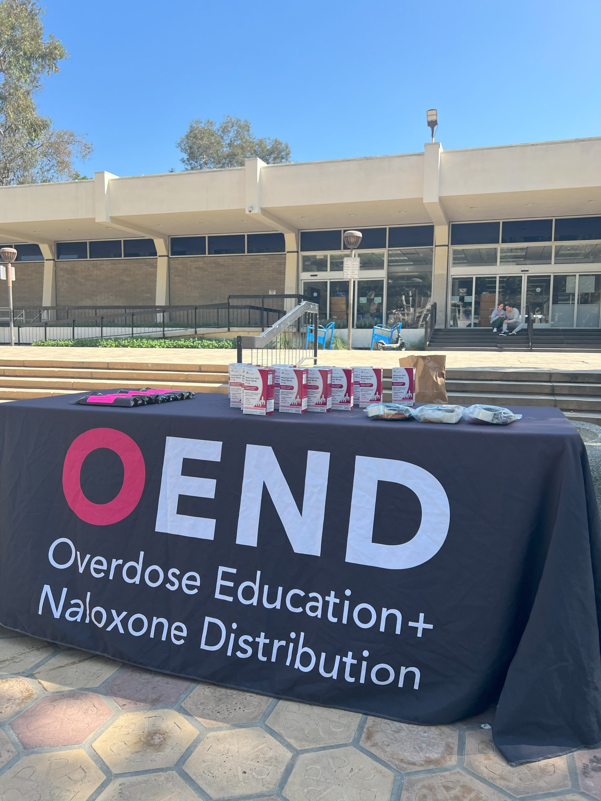 Naloxone access point table with overdose prevention supplies between the Pomona Library and LA County Courthouse.