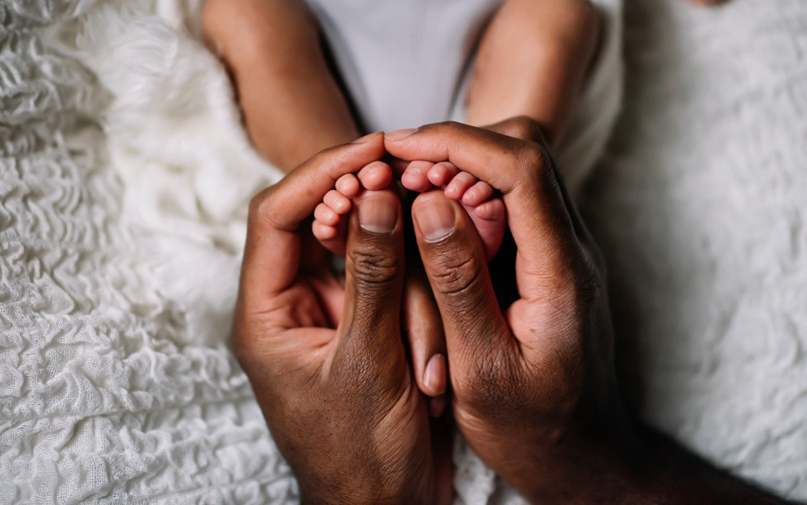 Adult hands gently holding a baby's tiny feet