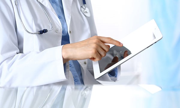 A close up photo of a person wearing a lab coat and holding and tablet computer.