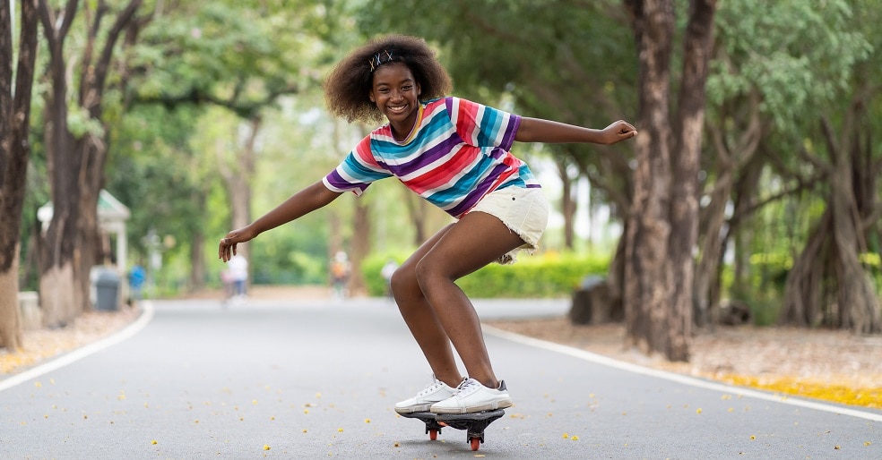 African American child girl having fun riding skateboard at summer outdoor. Teenager girl practicing skateboarding in the park.