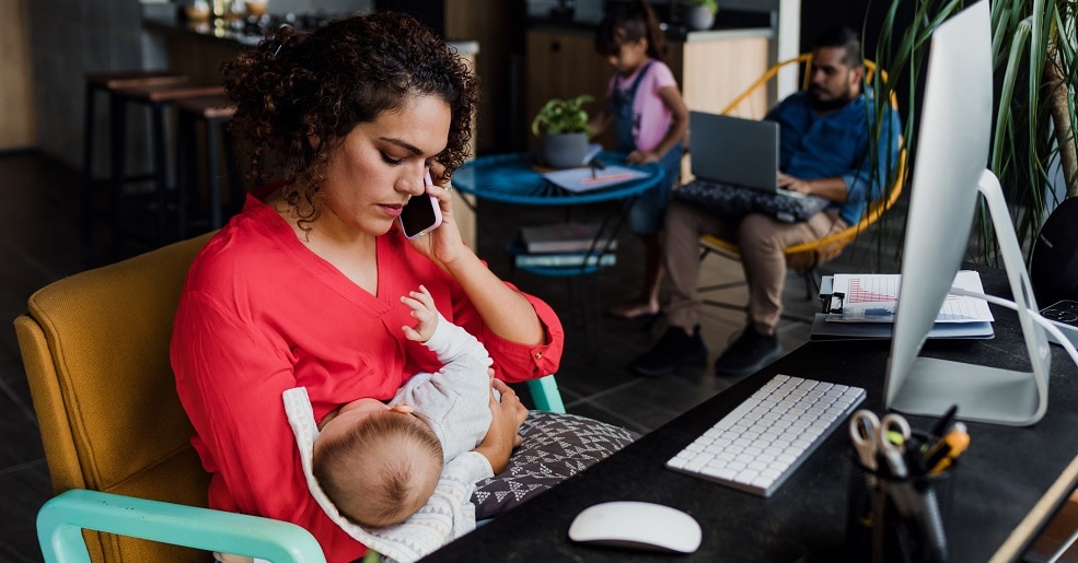 Mother holding baby while on the phone in front of a computer suggesting a dire emergency.