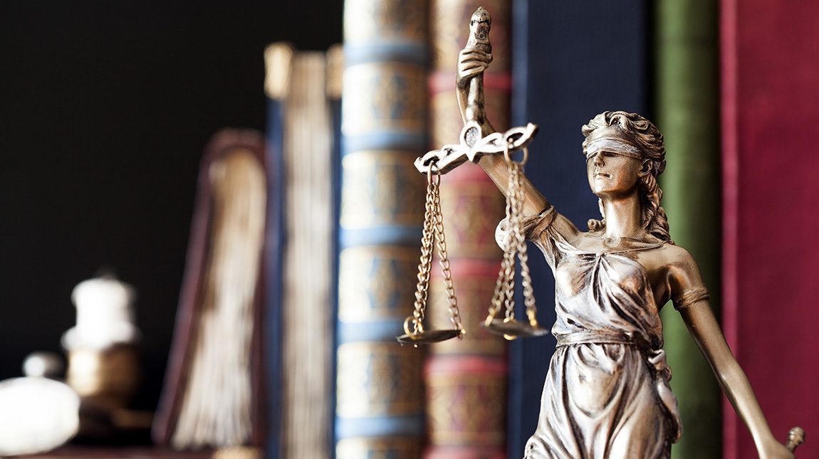 Lady justice statue holding scales with books in the background