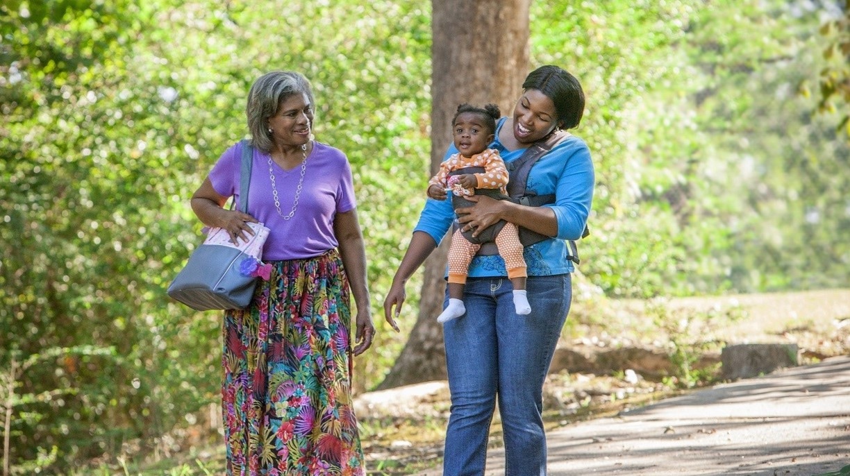 Two women and a baby walking together in a park.