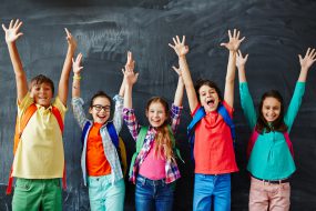 Five smiling students in front of a chalkboard stretching their arms over their heads.